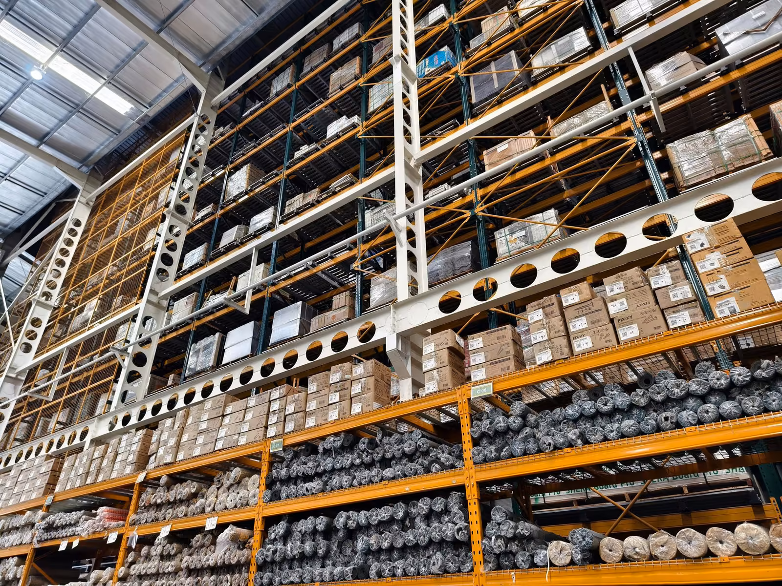 Warehouse shelves filled with stacked cardboard boxes and cylindrical items wrapped in plastic