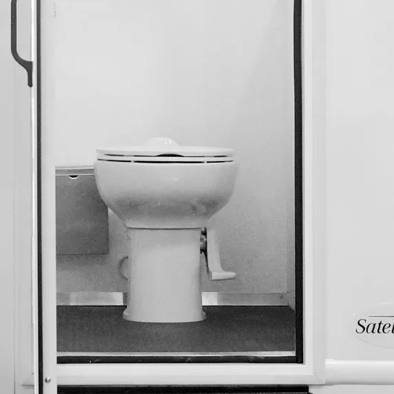 White flushing toilet inside portable restroom unit with closed door