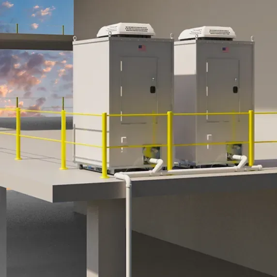 Two white portable sanitation units with air conditioning units on rooftop, installed on elevated concrete platform with yellow safety railing and visible plumbing