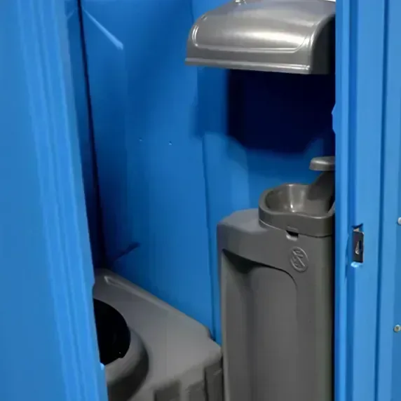 Interior of blue portable restroom showing handwash station and toilet seat with lid