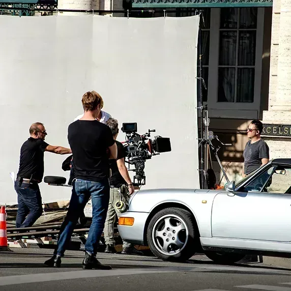 Film crew setting up camera equipment near silver sports car on street