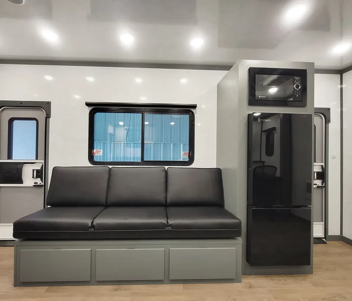 Black cushioned bench seat with gray storage base next to black microwave and refrigerator inside a mobile unit interior