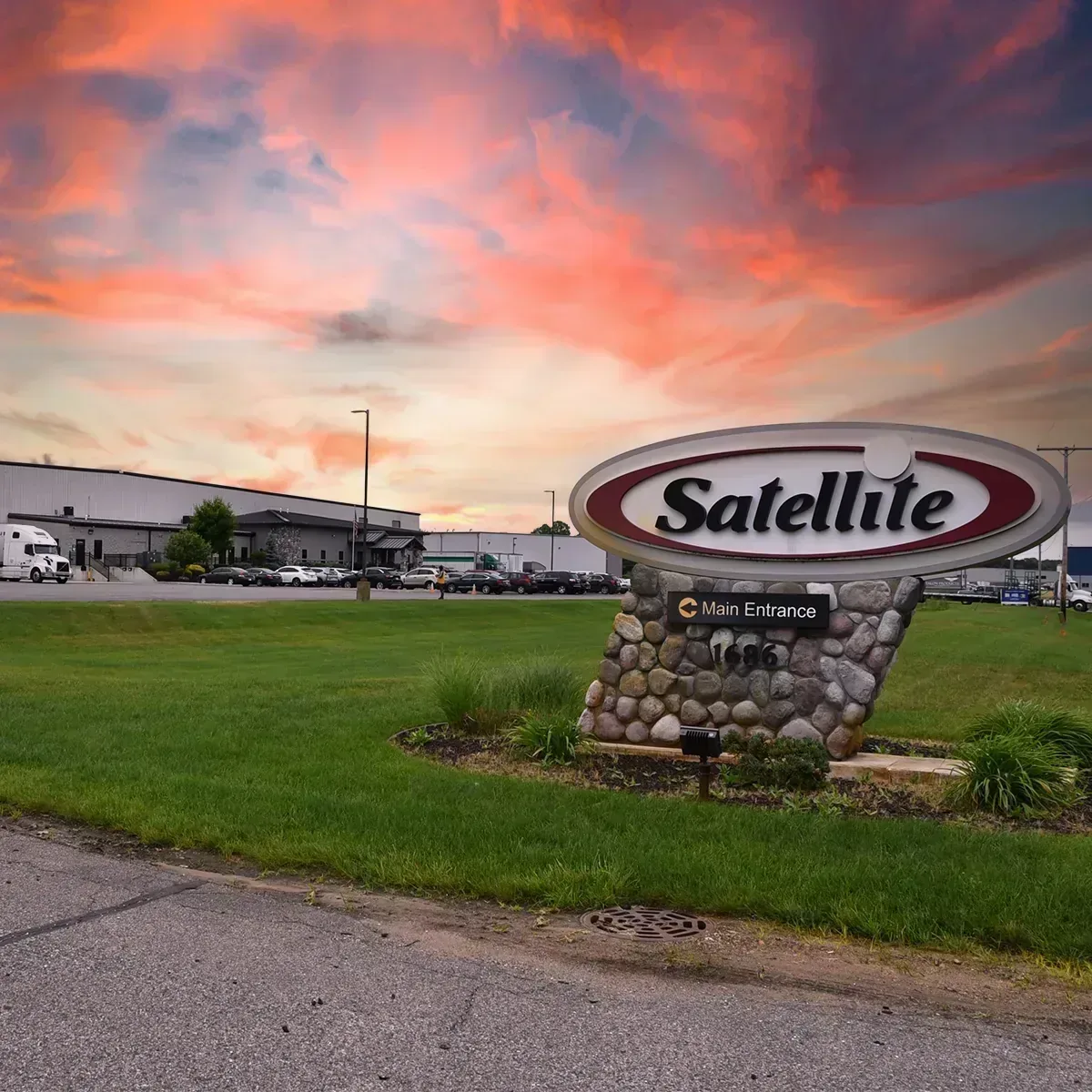 Satellite Industries stone monument sign with main entrance direction at facility parking lot during colorful sunset sky