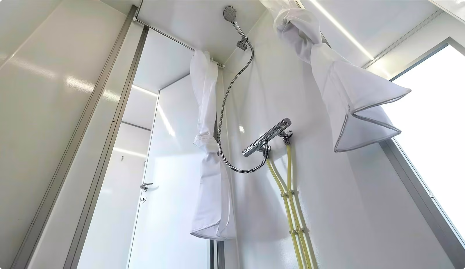 Shower interior with closed white curtain, hand-held showerhead, and visible temperature control with yellow hoses