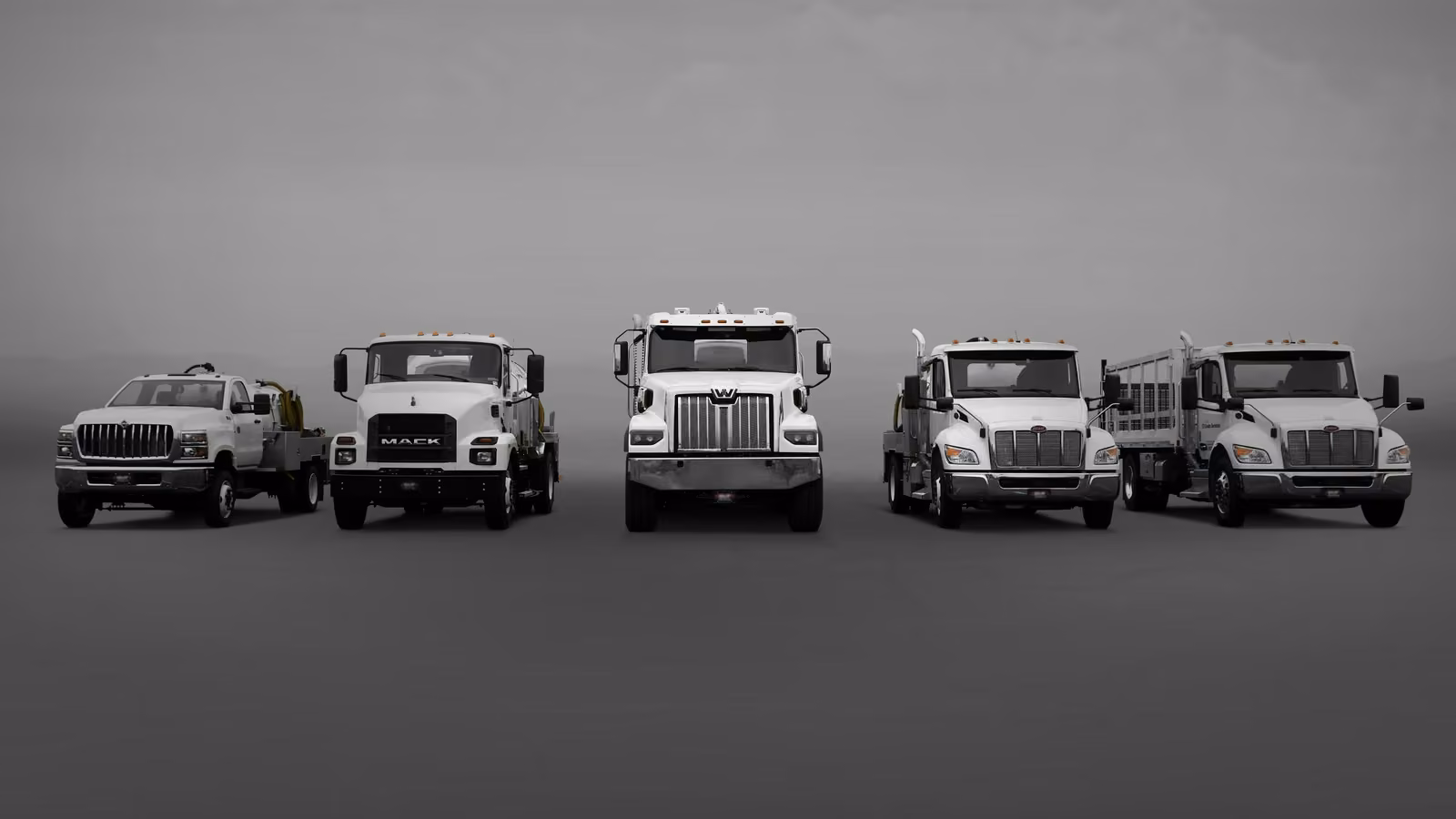 Five trucks lined up, varying in size and design, against a gray background.