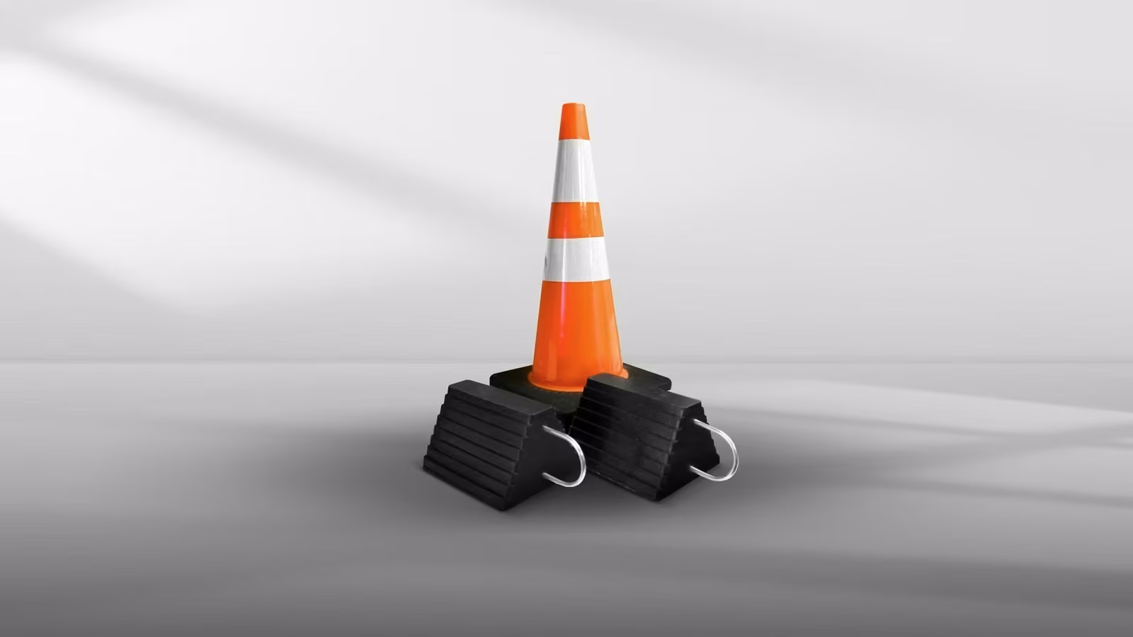 A traffic cone with white reflective stripes, positioned on two black rubber wheel chocks.