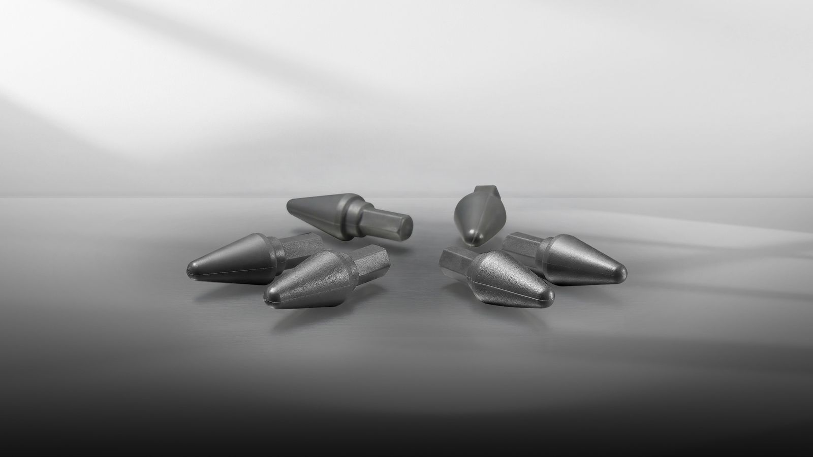 Six metallic screwdriver bits arranged on a reflective surface under soft lighting.