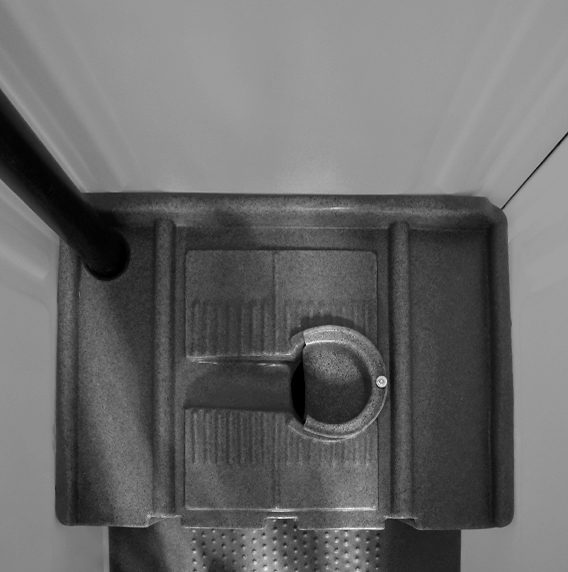 Black and white view from above of a floor drain with a circular catch in a textured surface.