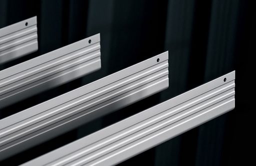 Four metallic strips with grooves and holes, arranged parallel against a dark background.