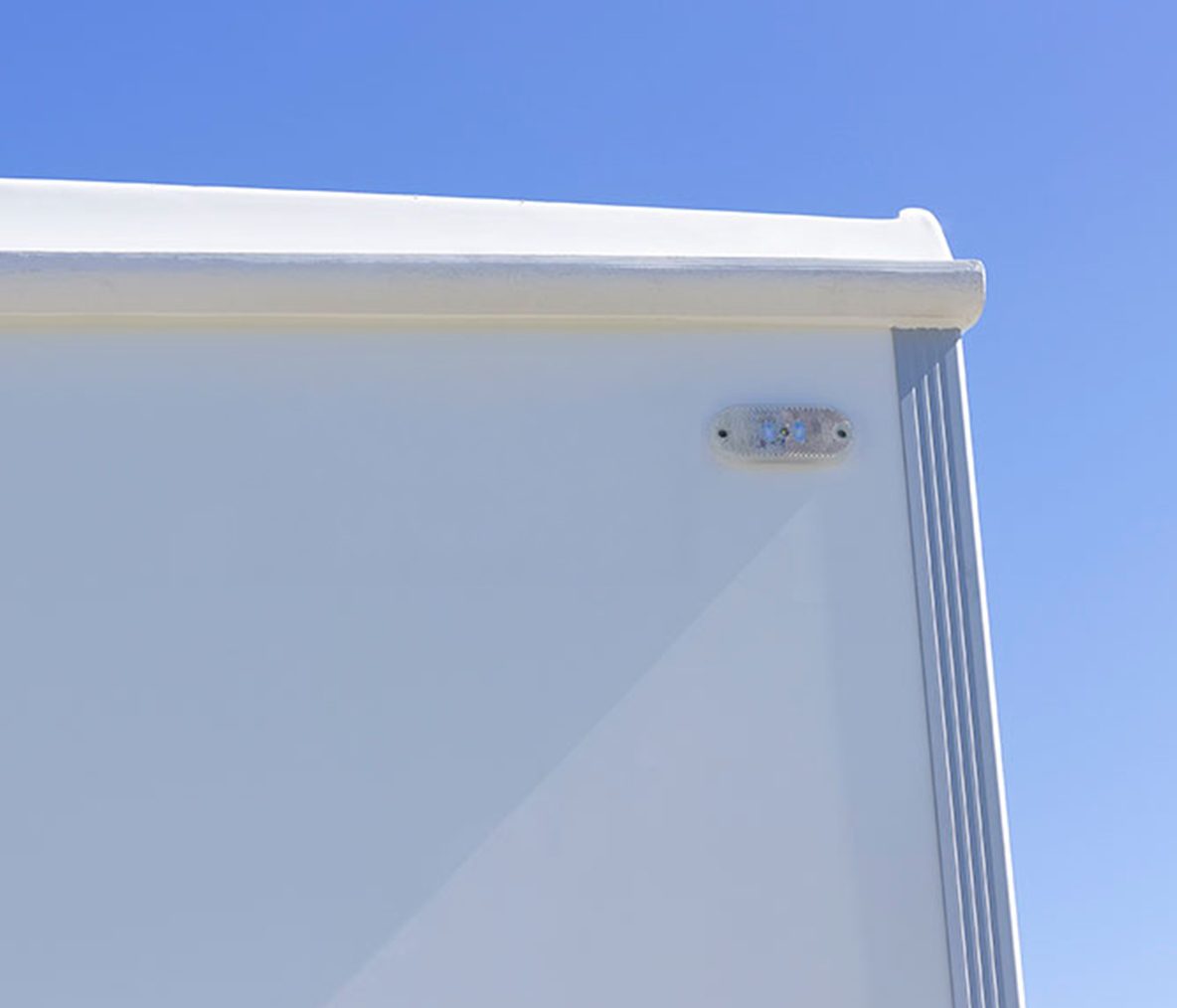 A white surface with a corner, featuring a small light fixture on the right side against a blue sky.